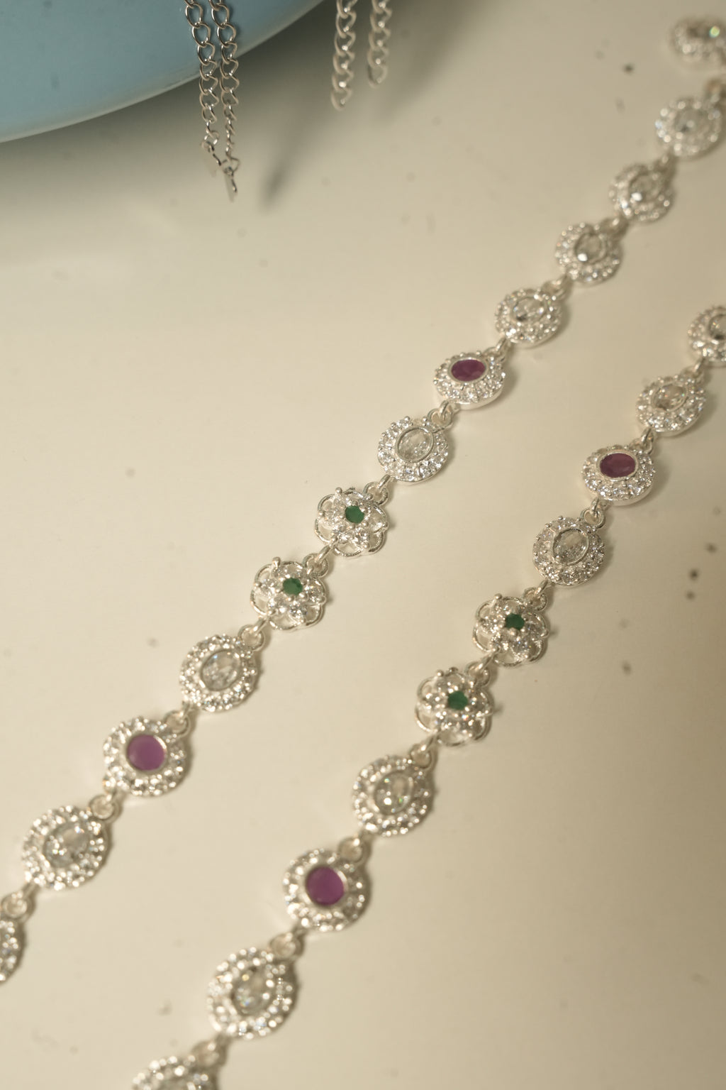 Angled view of the pair of payal, showing the deep pink stones and the flower links with green centres.