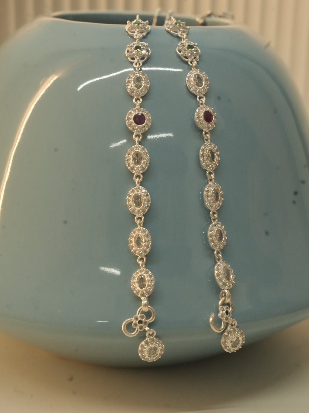 The pair of oval halo payal hanging over a blue vase, with the hook clasps and halo drops at the bottom.