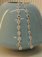 The pair of oval halo payal hanging over a blue vase, with the hook clasps and halo drops at the bottom.
