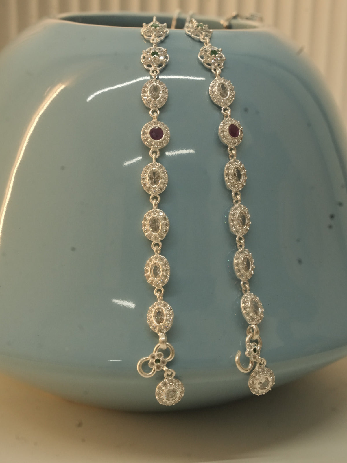 The pair of oval halo payal hanging over a blue vase, with the hook clasps and halo drops at the bottom.