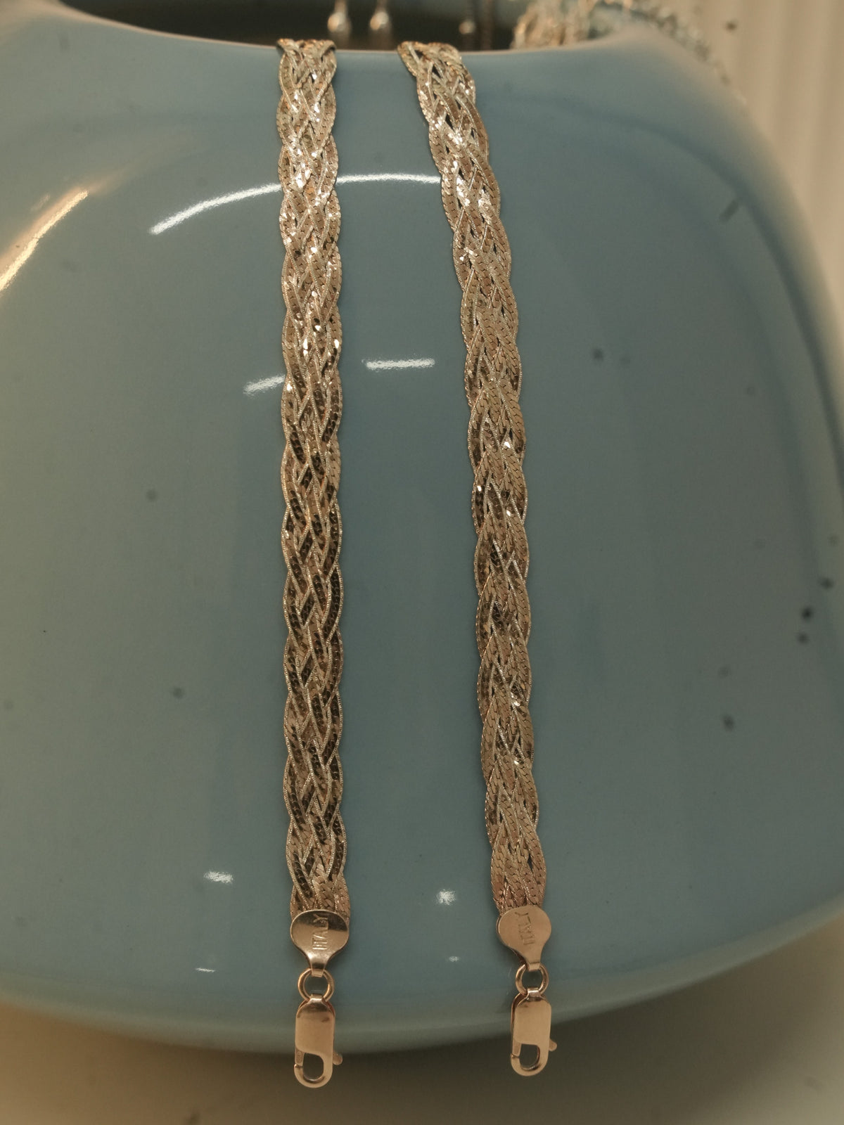 The rose gold plated braided herringbone payal draped over a blue ceramic vase, with the lobster clasps hanging below.