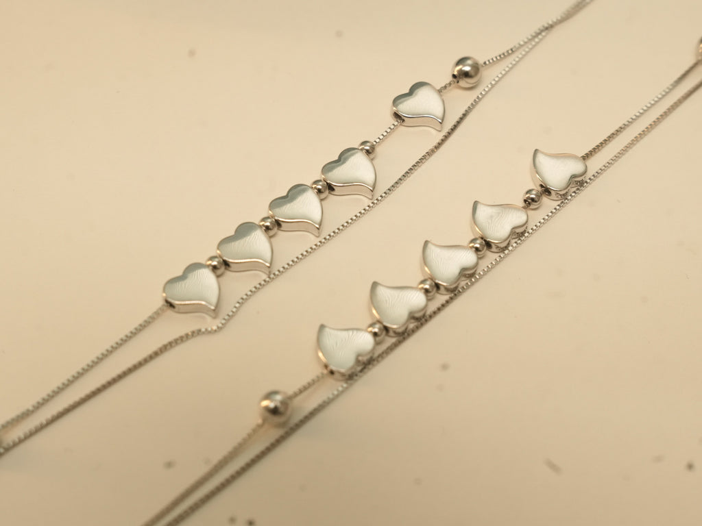 Close view of five polished silver hearts in a row on each of a pair of double strand payal.
