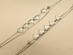Close view of five polished silver hearts in a row on each of a pair of double strand payal.