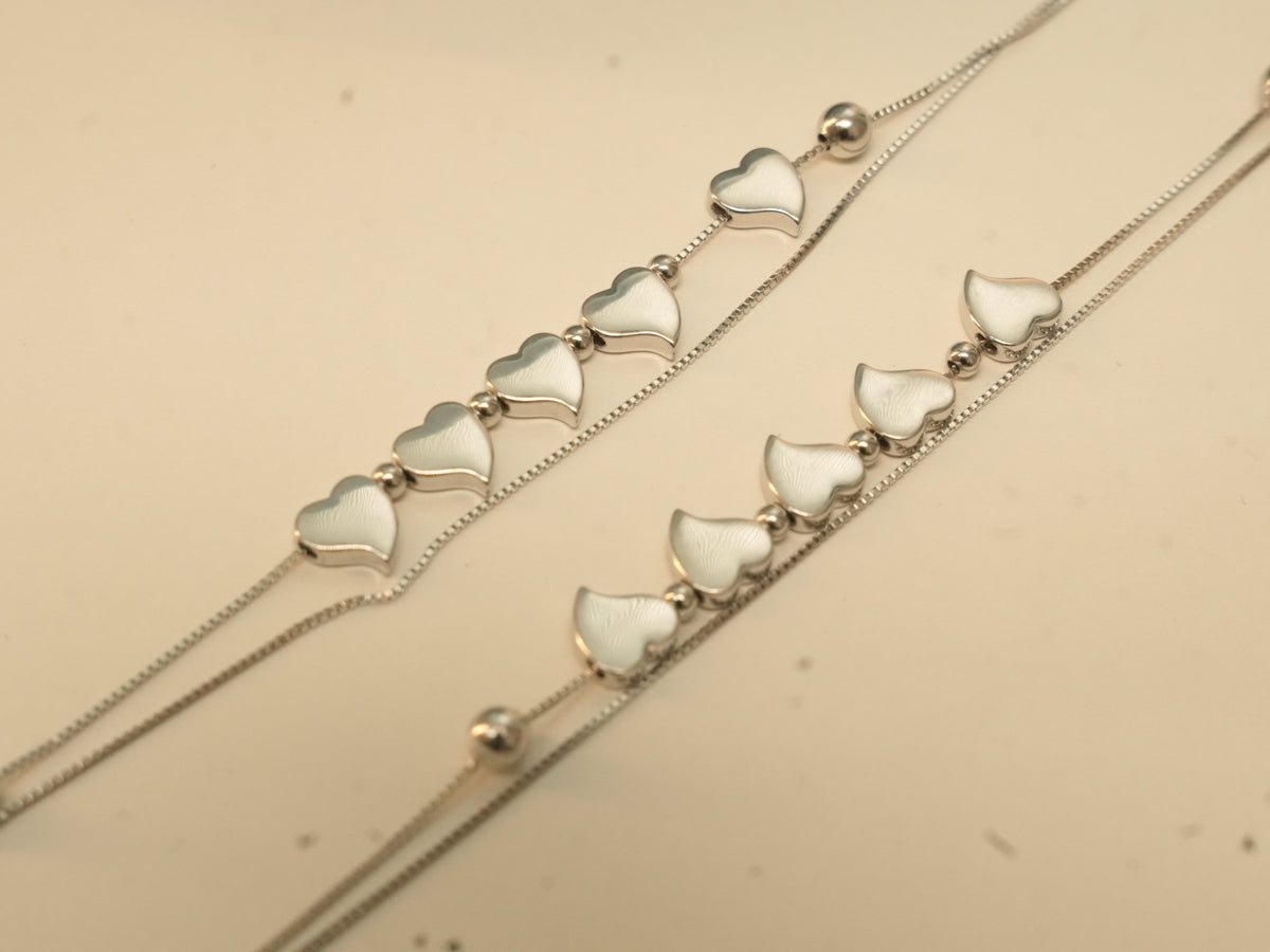 Close view of five polished silver hearts in a row on each of a pair of double strand payal.