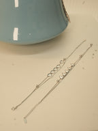 The pair of five heart silver payal laid out full length beside a blue vase.