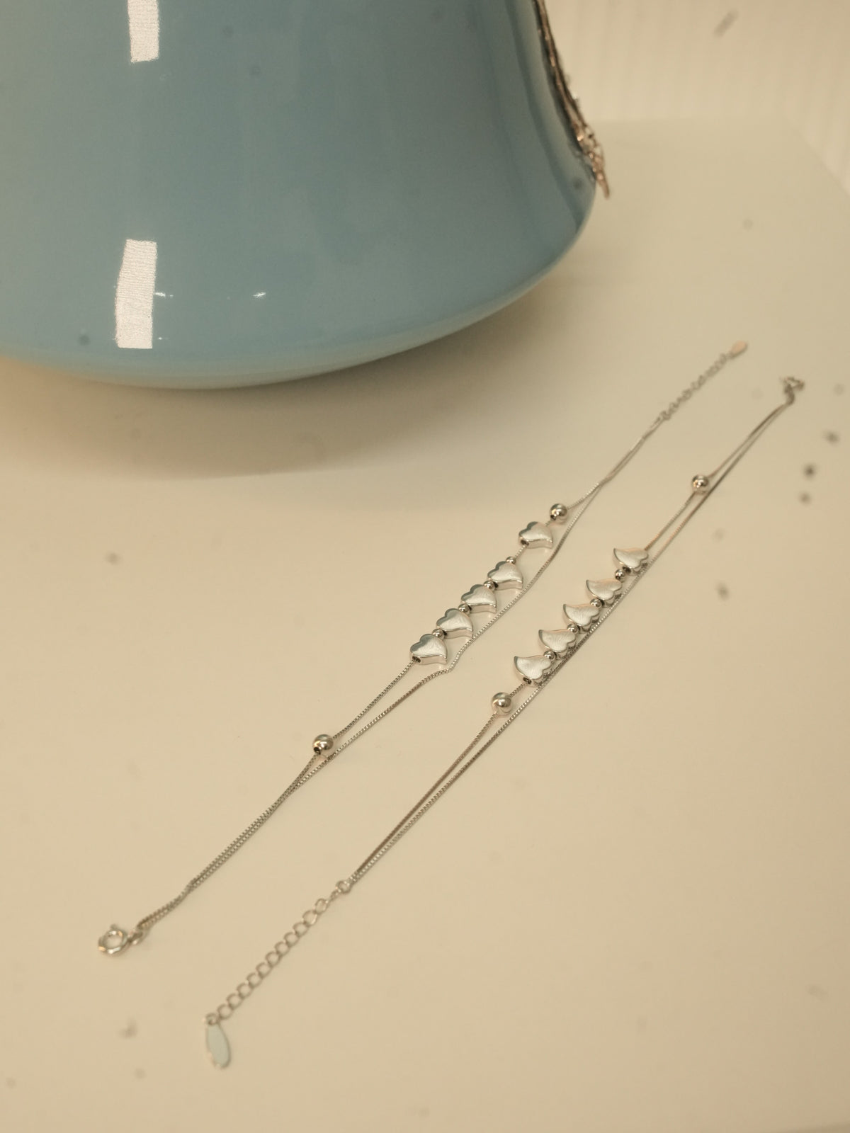 The pair of five heart silver payal laid out full length beside a blue vase.
