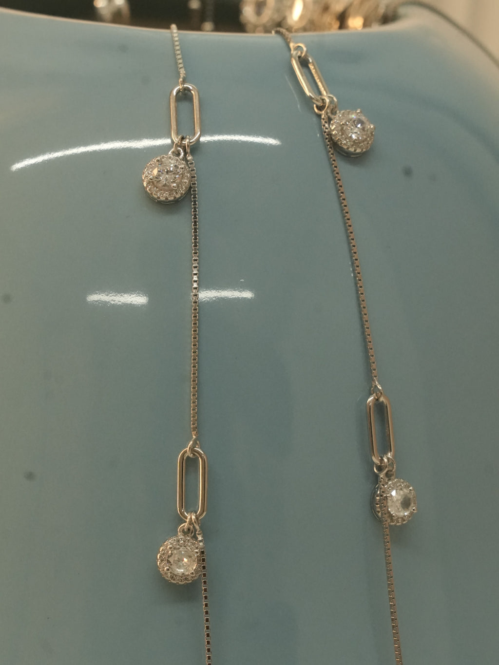 Close view of the paperclip links and American Diamond halo drops against a blue vase.