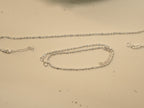 Pair of plain silver payal in a bar and bead chain, one laid straight and one coiled.