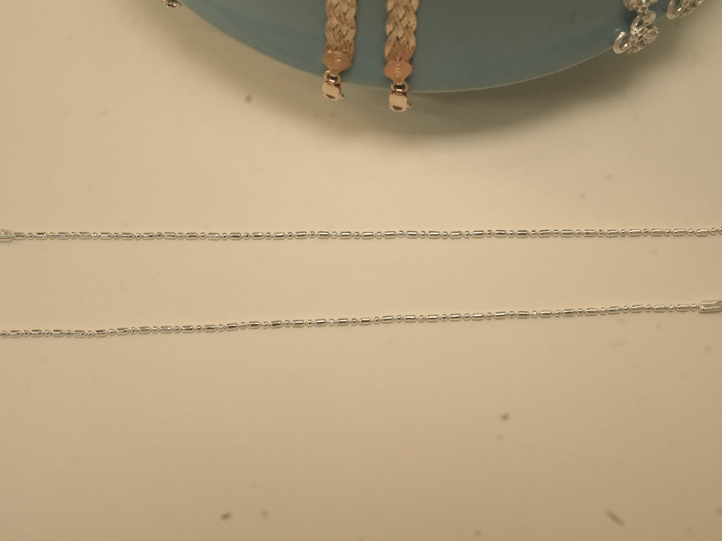 The pair of bar and bead silver payal laid out full length.