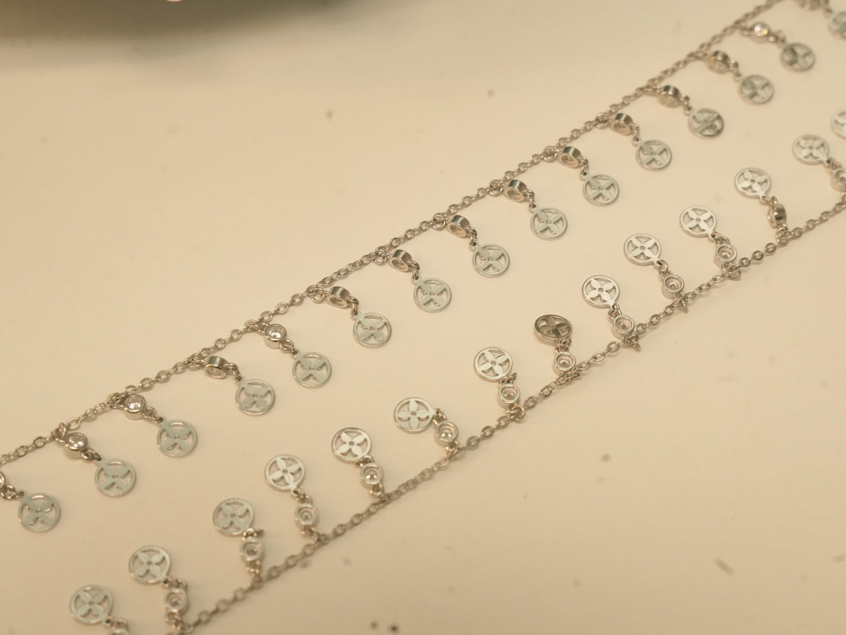 Close view of the round discs pierced with four petal flowers on the silver payal.