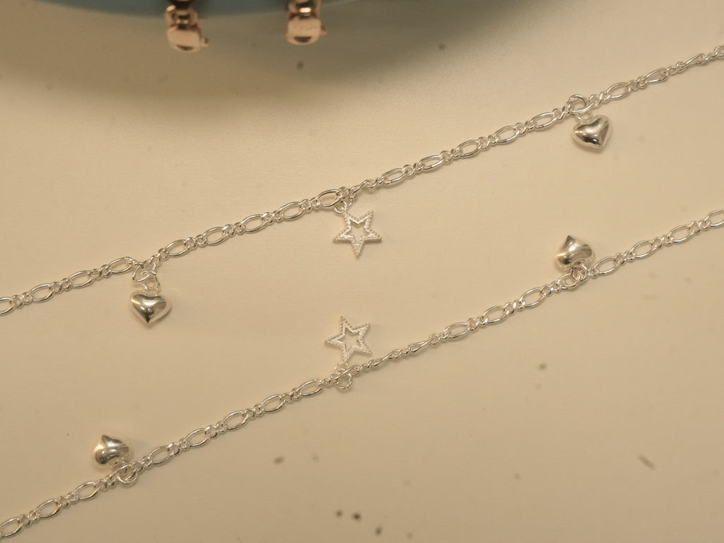 Pair of silver figaro chain payal, each with puffed heart charms and an open star.