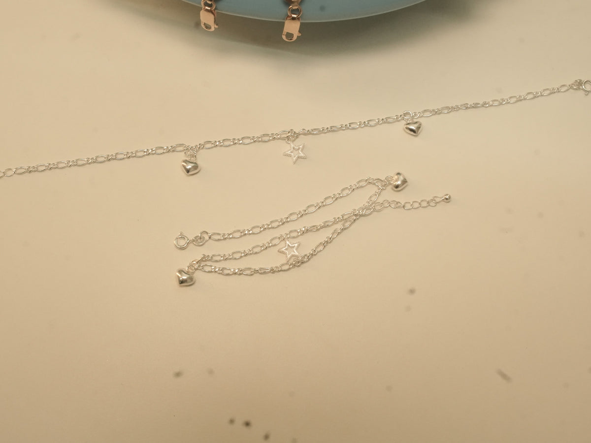One heart and star payal laid straight and the other coiled, showing the clasp and extender chain.