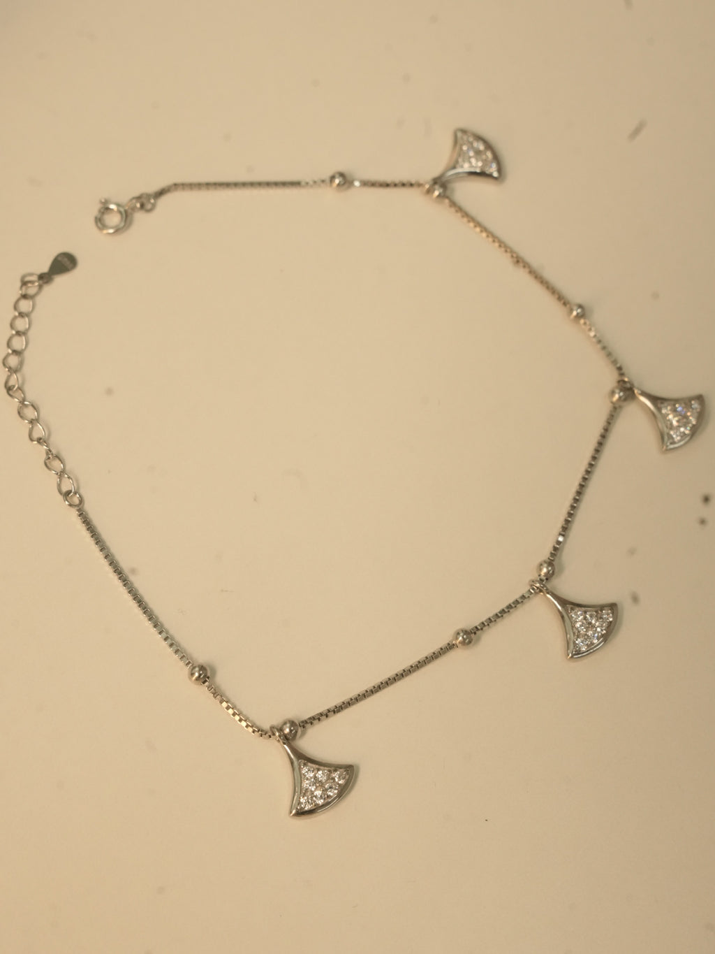 The fan charm anklet laid in a loop, showing the spring ring clasp and the extender chain.