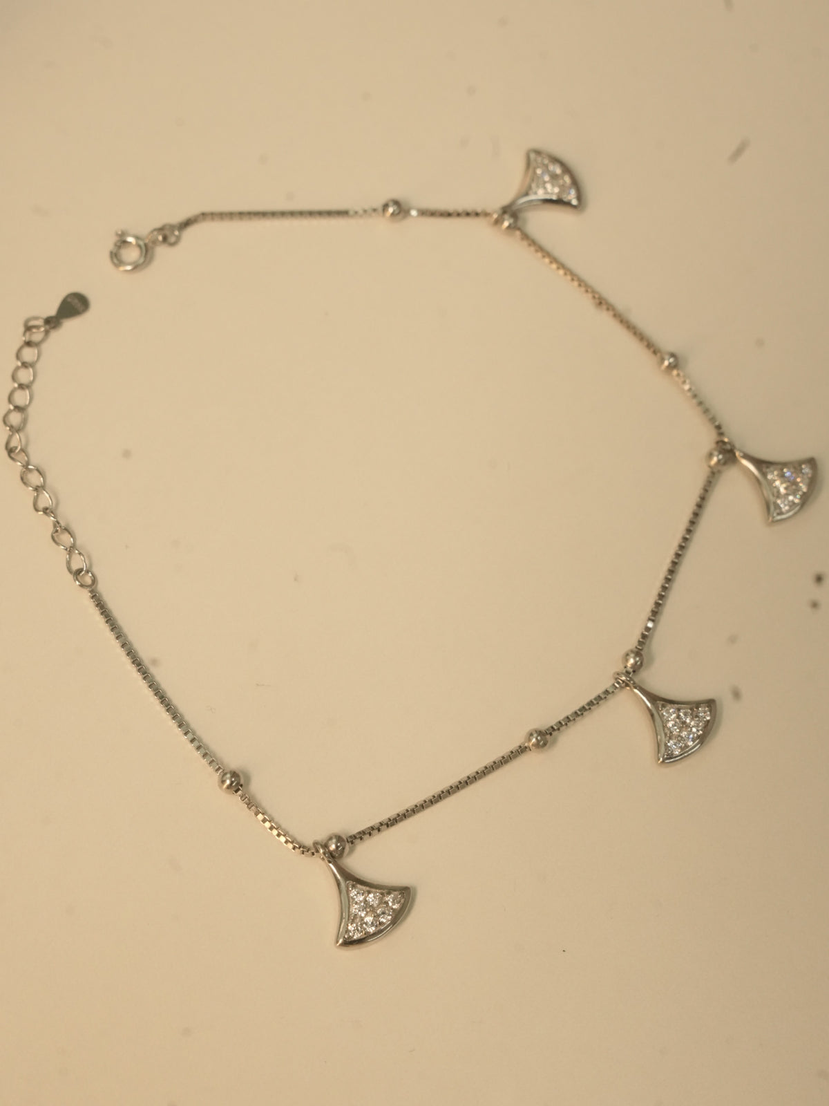 The fan charm anklet laid in a loop, showing the spring ring clasp and the extender chain.