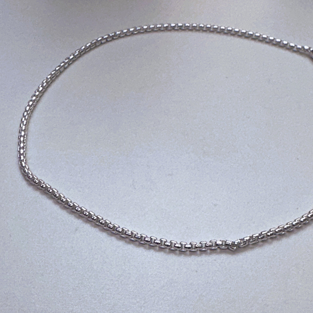 The round box chain anklet laid in a loop to show the even links along its length.