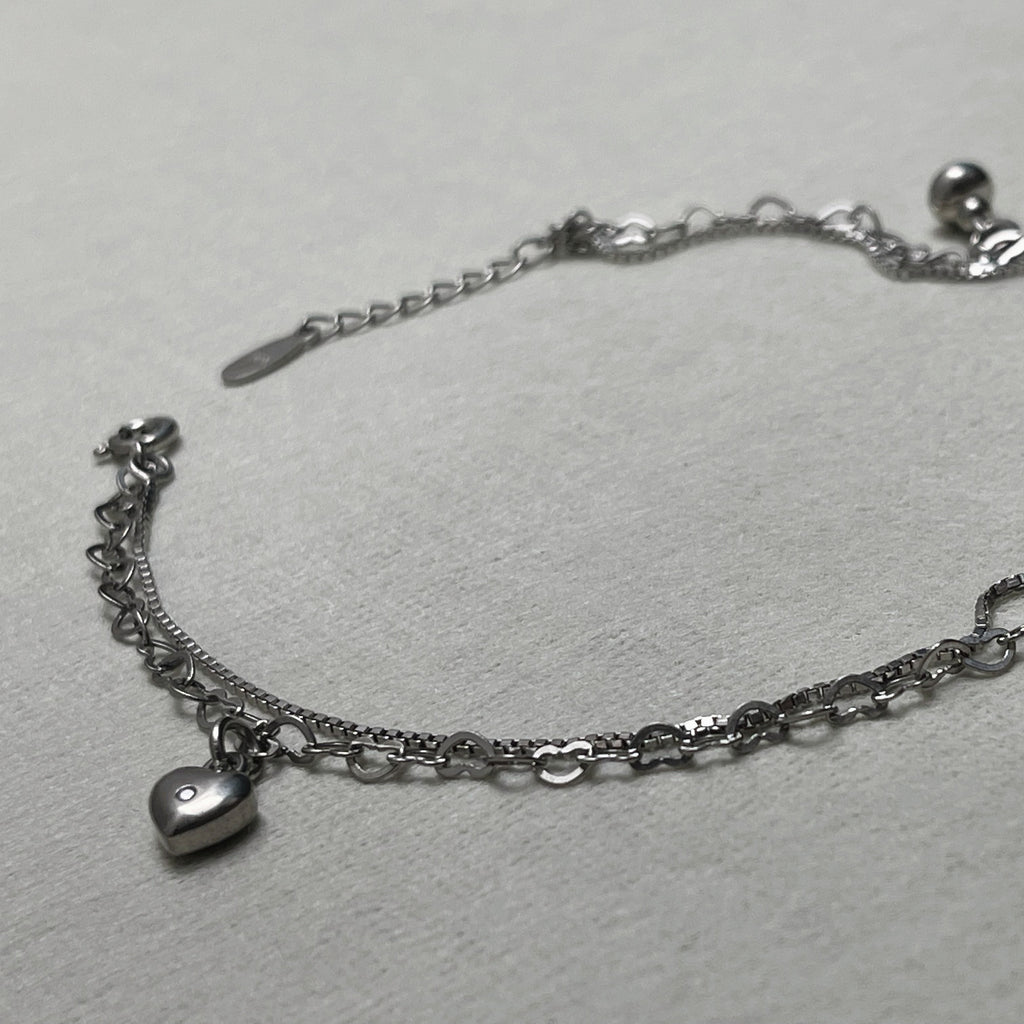 The two strands of the anklet, box chain and heart links, laid out with the heart charm and extender chain.