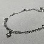 The two strands of the anklet, box chain and heart links, laid out with the heart charm and extender chain.