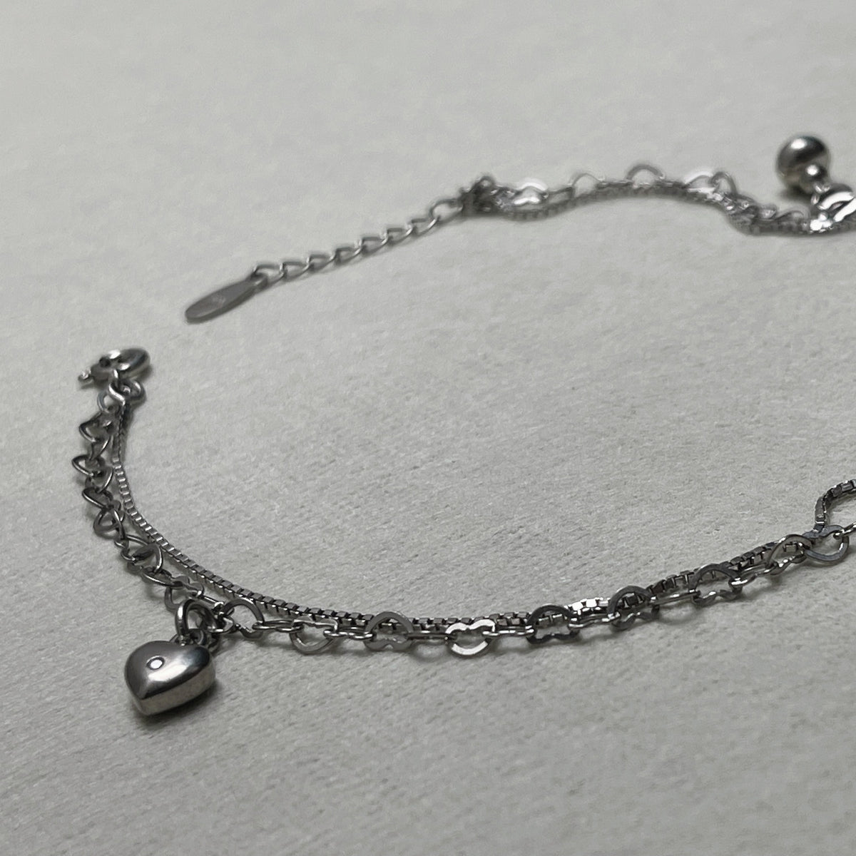 The two strands of the anklet, box chain and heart links, laid out with the heart charm and extender chain.
