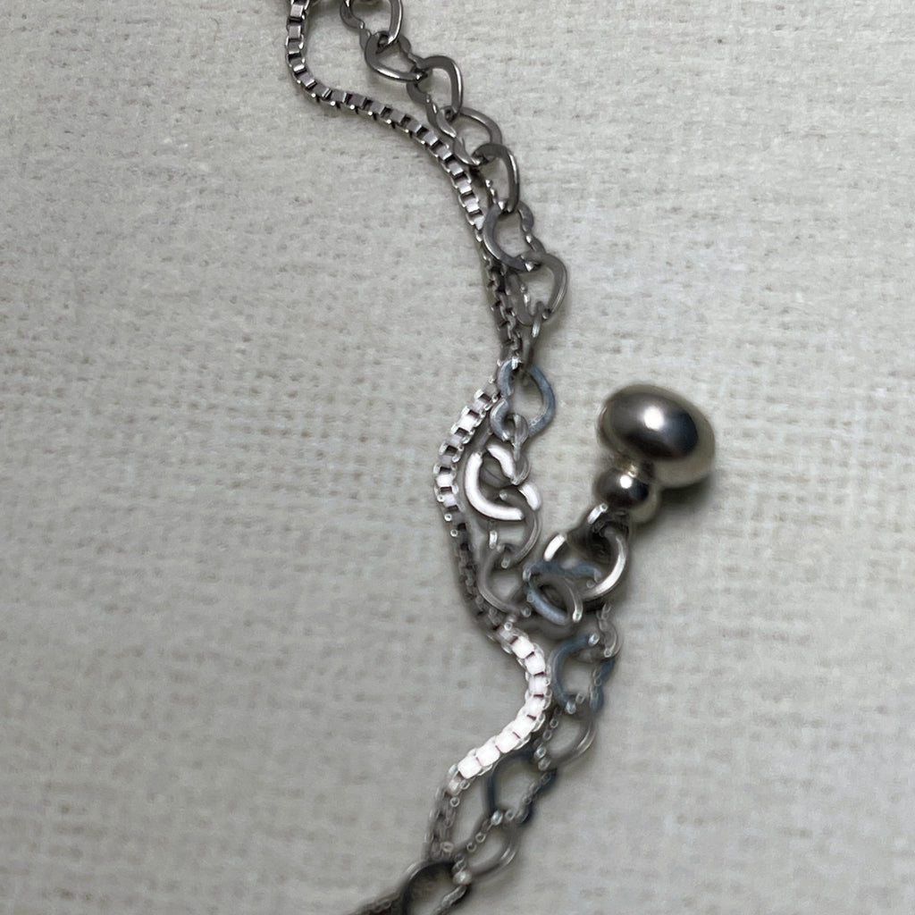 Close-up of the polished silver ball charm where the two chains meet.