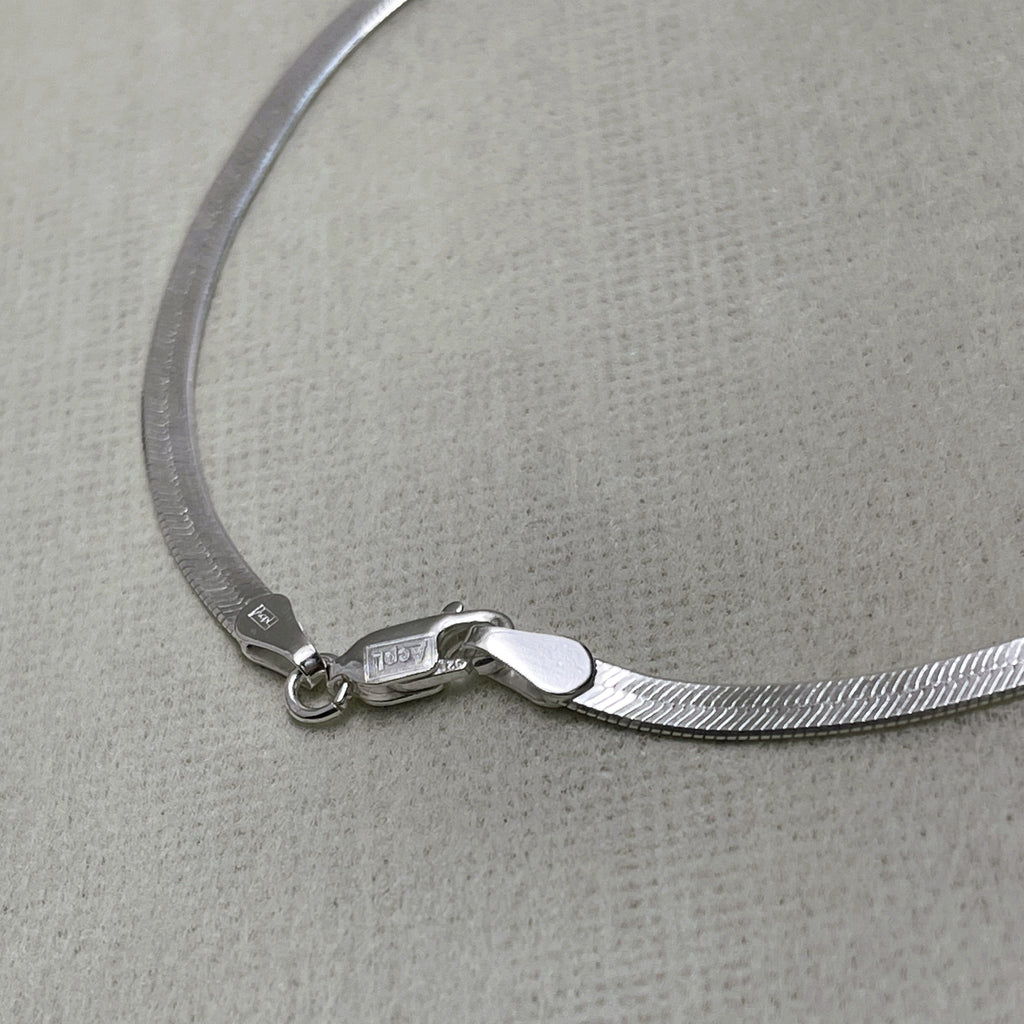 Close-up of the herringbone links and the lobster clasp of the silver anklet.