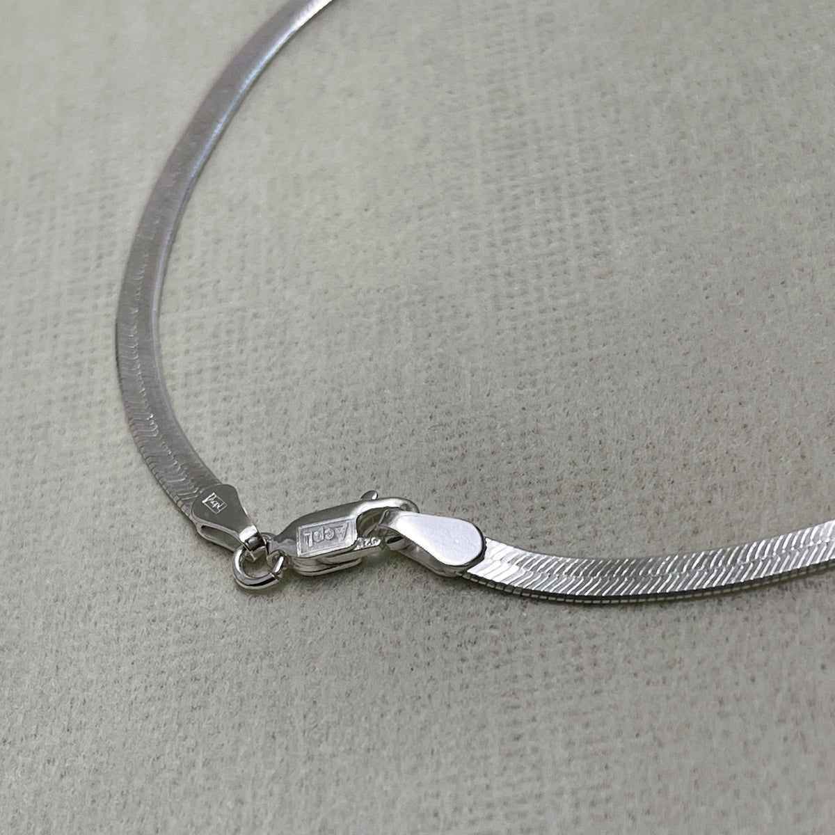 Close-up of the herringbone links and the lobster clasp of the silver anklet.