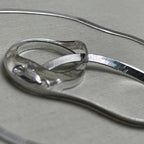The flat herringbone silver anklet coiled to show the smooth ribbon of links.