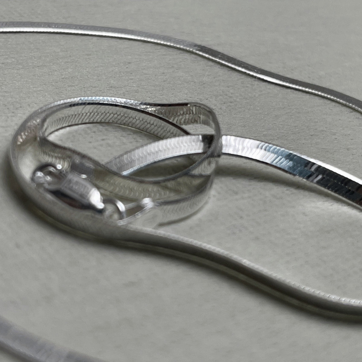 Pair of flat herringbone silver payal: one anklet coiled to show the smooth ribbon of links.