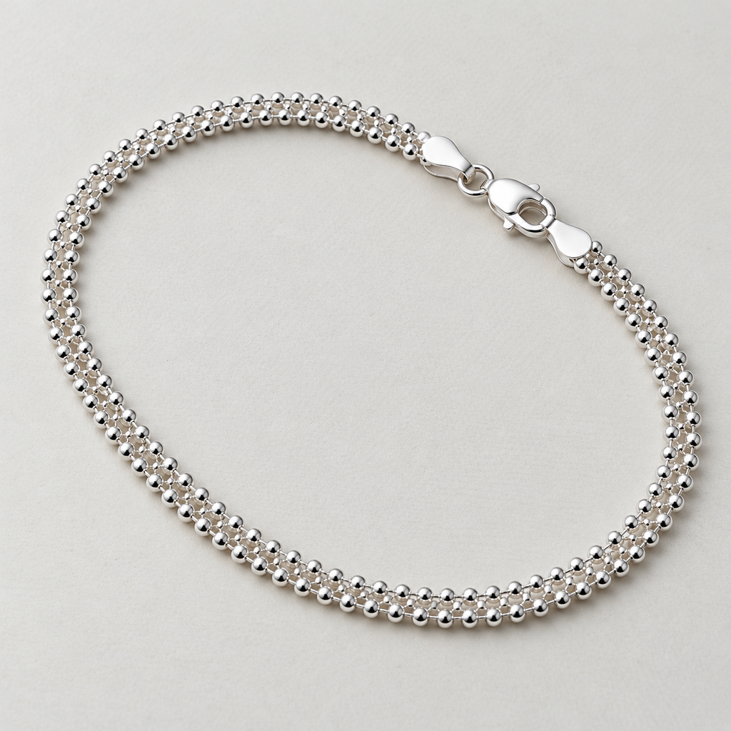 Sterling silver popcorn chain anklet laid in a loop with its lobster clasp, on a cream surface.