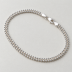 Sterling silver popcorn chain anklet laid in a loop with its lobster clasp, on a cream surface.