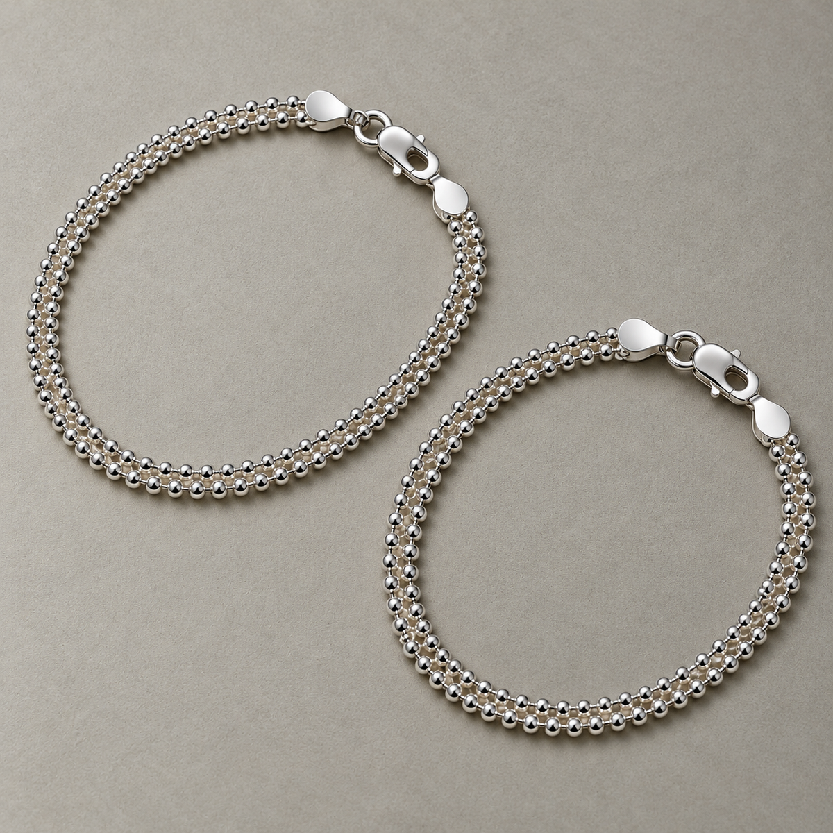 A pair of sterling silver popcorn chain anklets laid side by side.