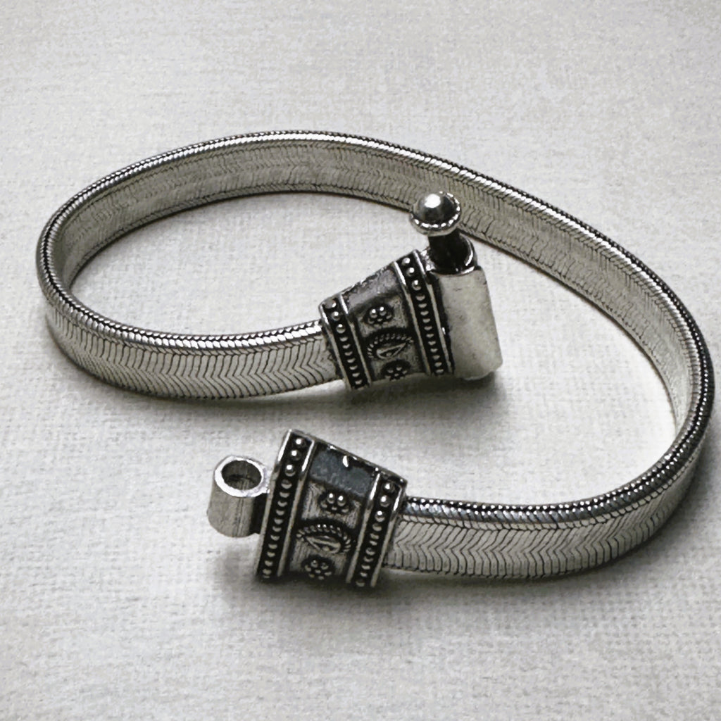 Rajwadi sterling silver payal, a wide flat snake chain with carved oxidised end caps, laid in a loop with the pin clasp open.