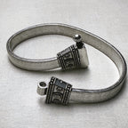 Rajwadi sterling silver payal, a wide flat snake chain with carved oxidised end caps, laid in a loop with the pin clasp open.
