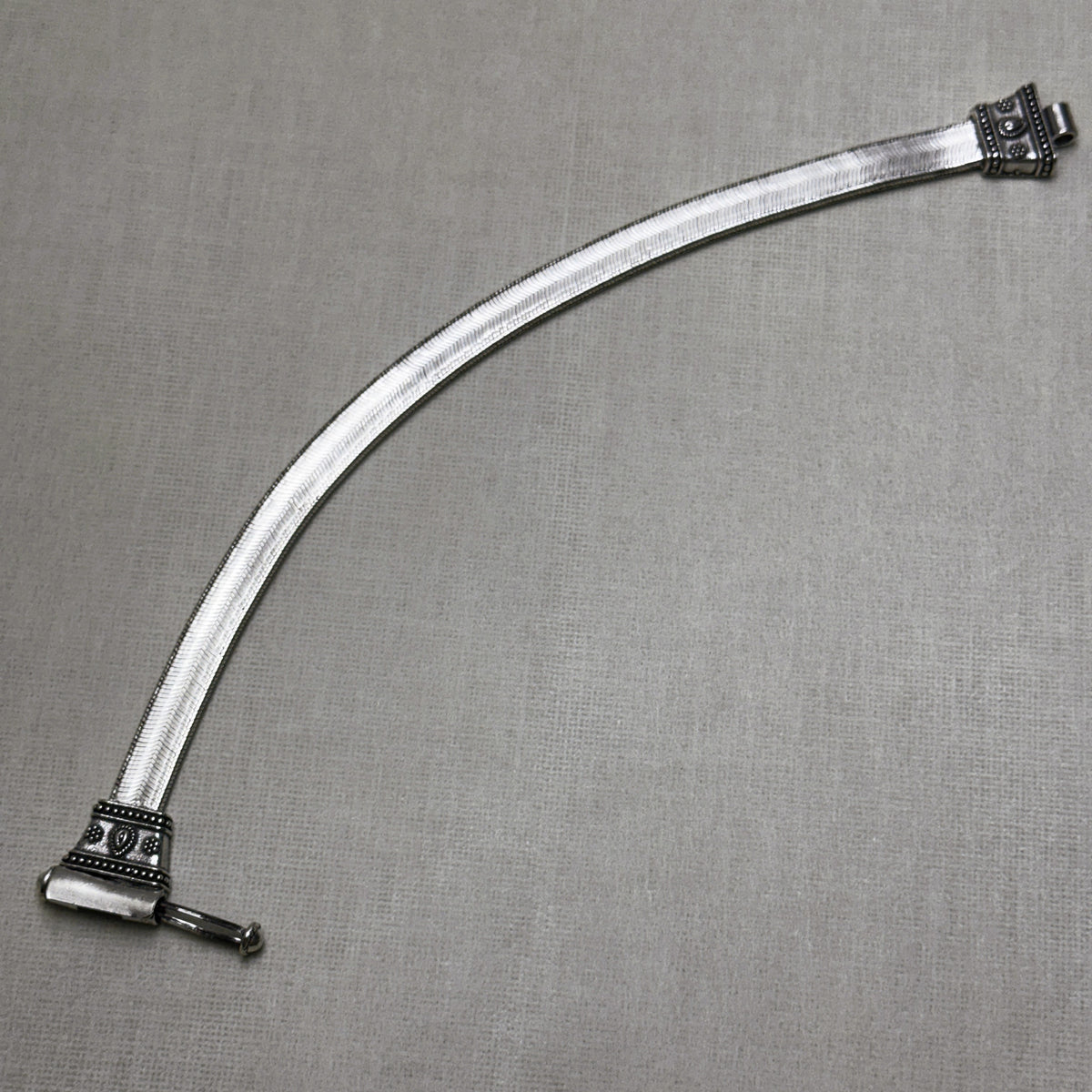 The rajwadi silver payal laid out straight, with the carved caps and pin at each end.