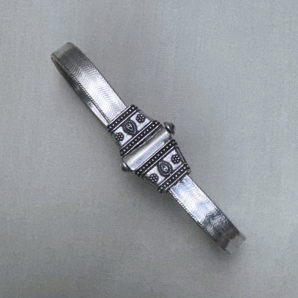 The oxidised carved end cap of the silver anklet, with its beaded borders and leaf motif.
