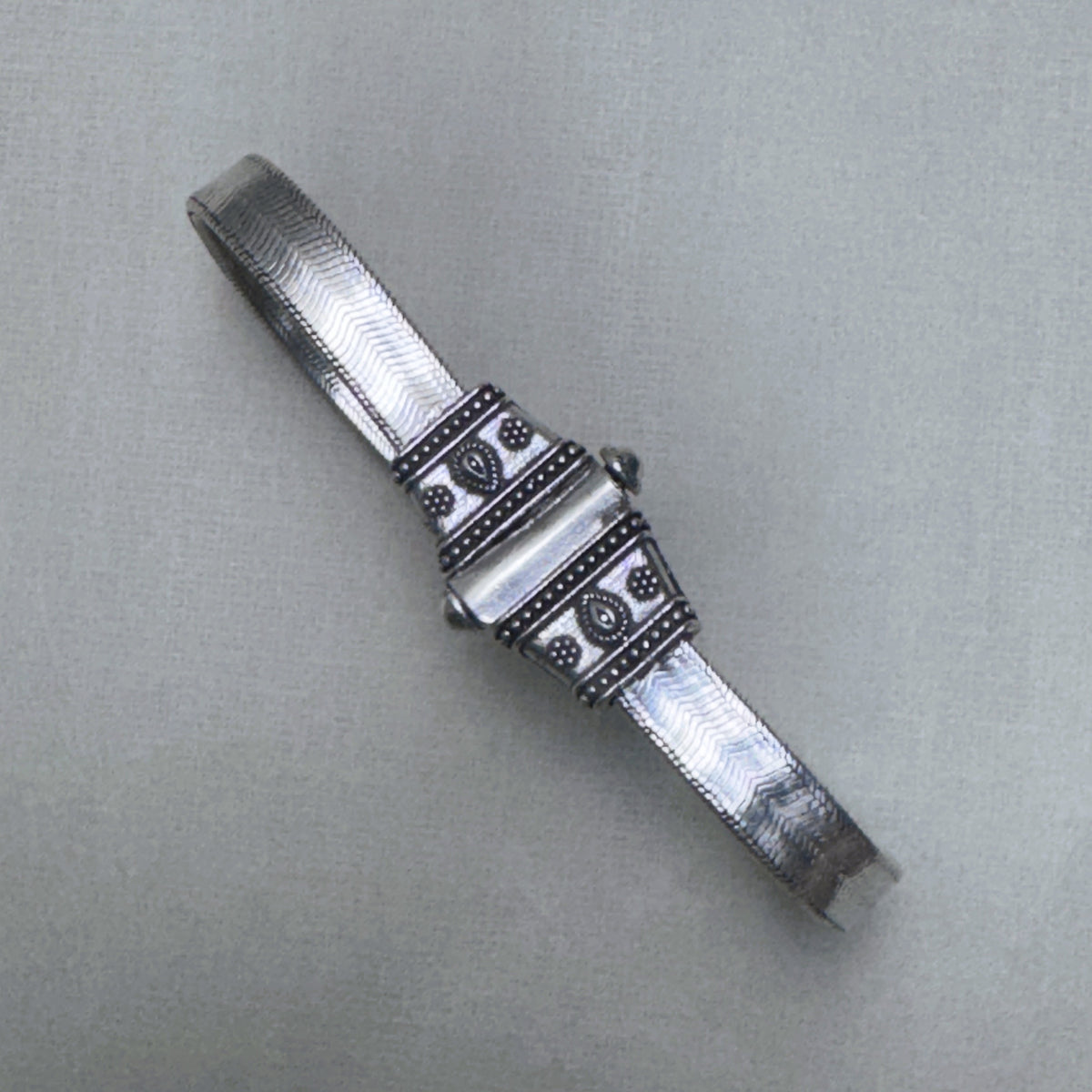 The oxidised carved end cap of the silver anklet, with its beaded borders and leaf motif.
