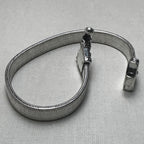 The wide flat snake chain anklet in a loop, showing the two carved caps and the pin clasp.