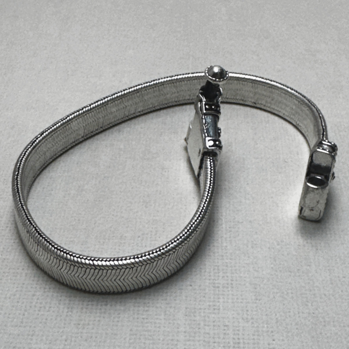 The wide flat snake chain anklet in a loop, showing the two carved caps and the pin clasp.