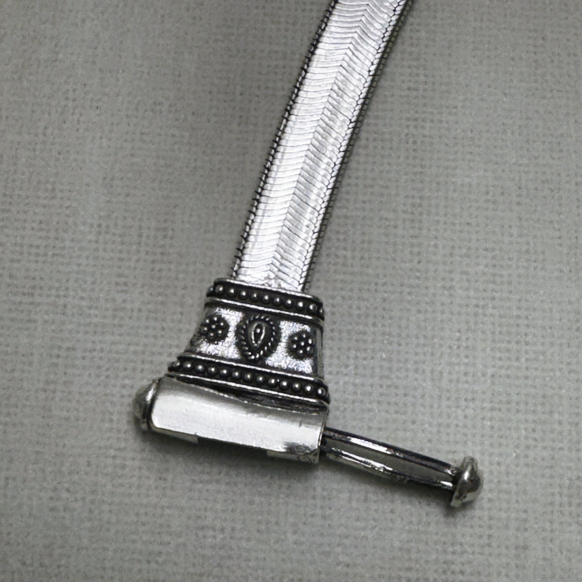 The pin of the clasp drawn out, showing how the bar slides through the barrel.