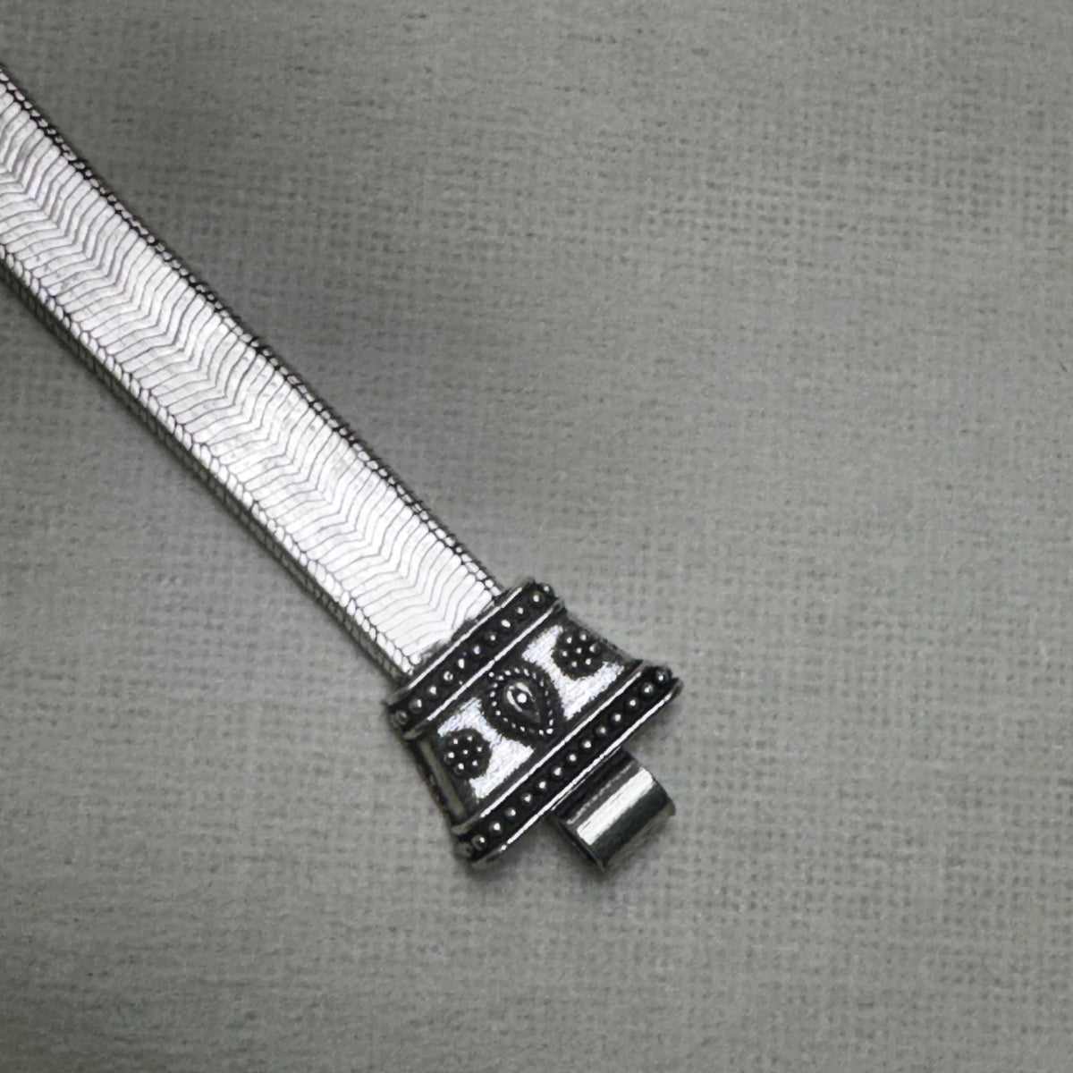 The second carved cap of the anklet with its slot for the pin, on the flat snake chain.