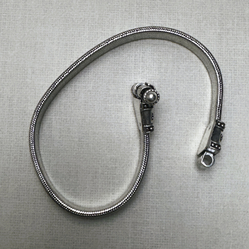 The flat snake silver anklet seen on its edge, coiled, with the clasp caps at the top.