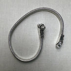 The flat snake silver anklet seen on its edge, coiled, with the clasp caps at the top.