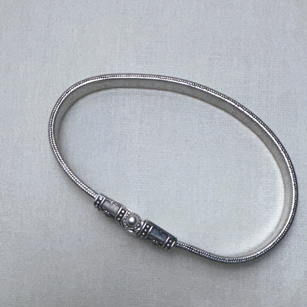 The flat snake silver anklet laid in a full loop with the clasp closed.