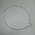 Sterling silver round snake chain anklet laid in a loop with its spring ring clasp, on a grey surface.