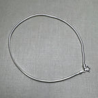 Sterling silver round snake chain anklet laid in a loop with its spring ring clasp, on a grey surface.