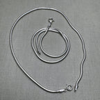 A pair of round snake chain silver anklets, one coiled inside the other.