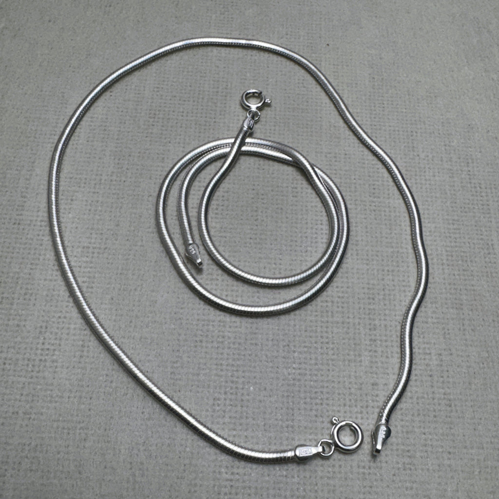 A pair of round snake chain silver payal, one coiled inside the other.