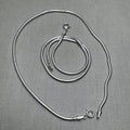 A pair of round snake chain silver payal, one coiled inside the other.
