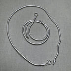 A pair of round snake chain silver payal, one coiled inside the other.