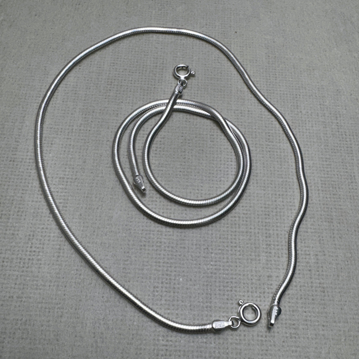 A pair of round snake chain silver payal, one coiled inside the other.