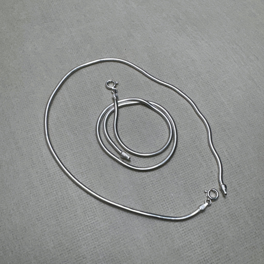The pair of round snake chain silver anklets with both spring ring clasps showing.